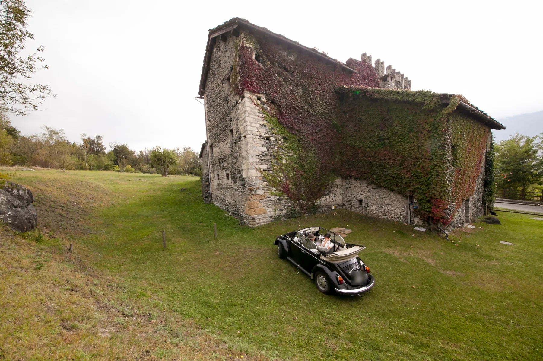 Maggiolino cabriolet degli sposi davanti a una casaforte coperta di vite
