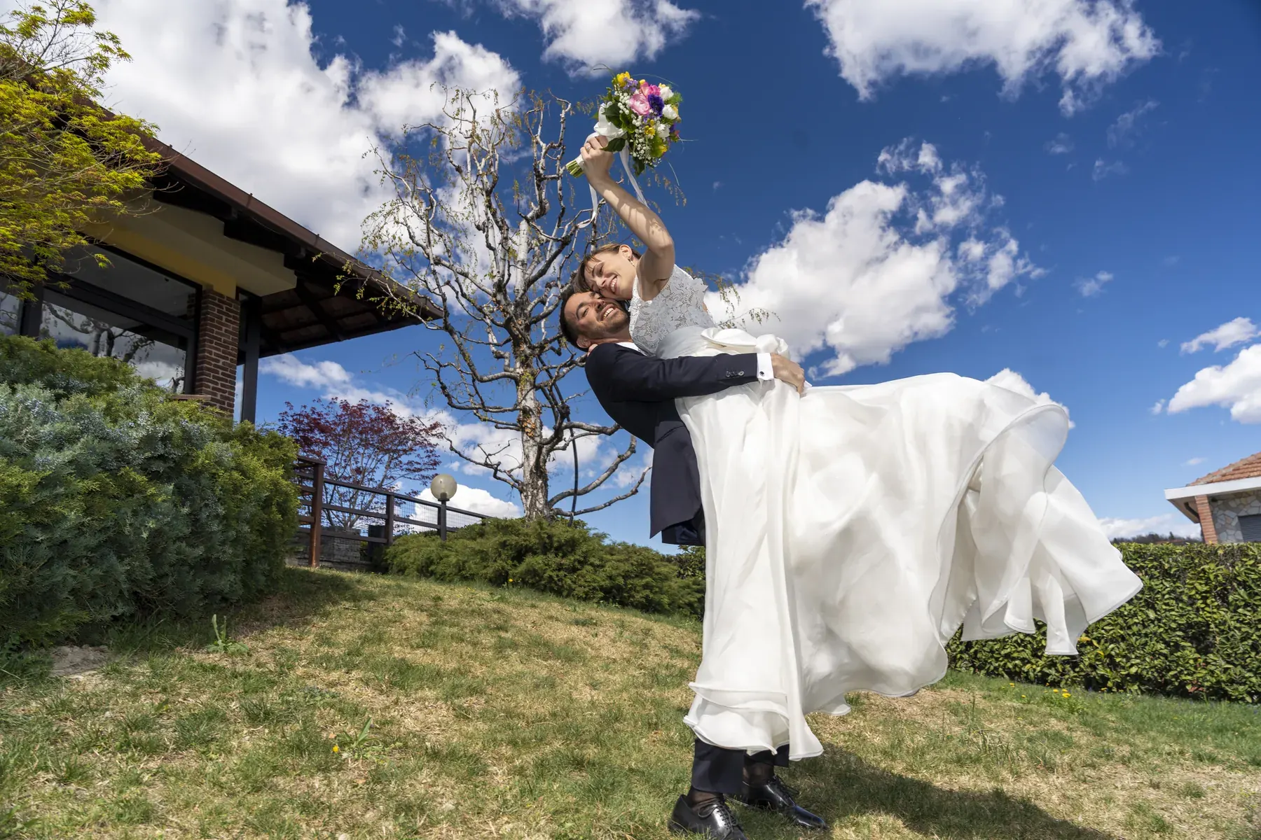Sposo che solleva la sposa sotto un cielo azzurro