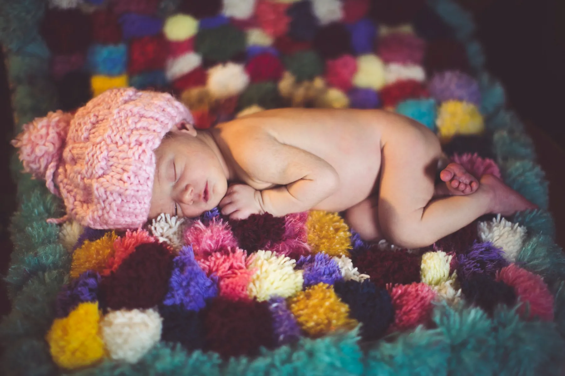 Neonata che dorme con cuffia rosa su una coperta di pompon